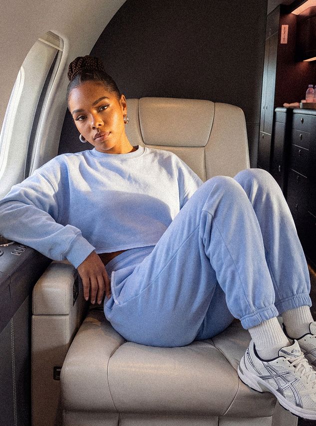 Mujer con sudadera corta y joggers azul claro, sentada cómodamente en un jet privado. Loungewear ideal para viajar.
