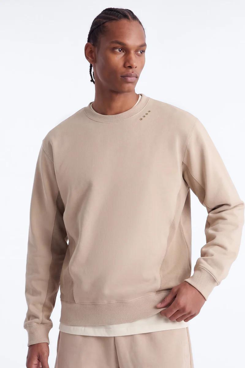 Man models a stylish tan crew neck sweatshirt with unique eyelets. Perfect for men's modern casual wear, highlighting new collection comfort.