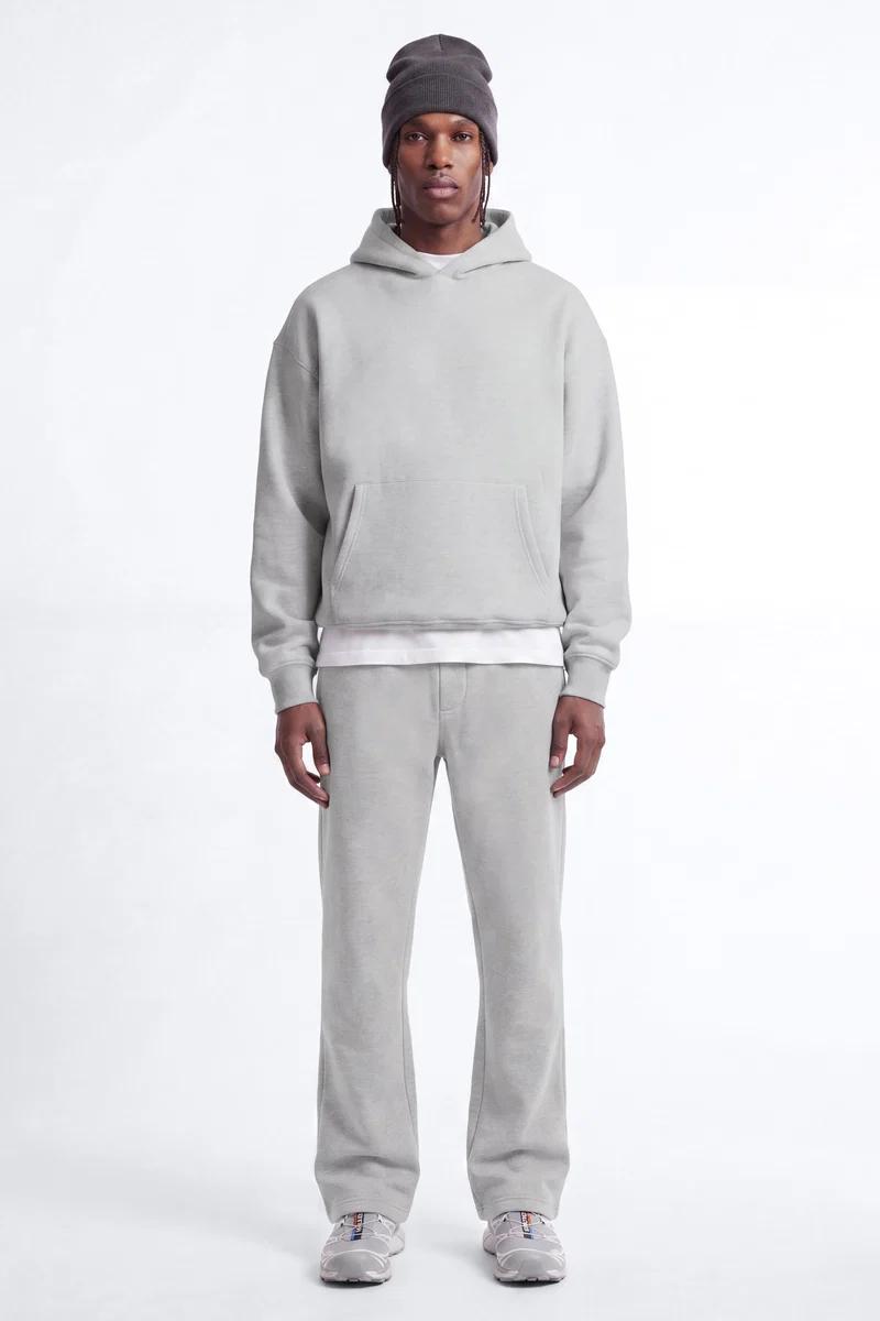Man modeling a relaxed light grey hoodie, matching sweatpants, grey beanie, and sneakers, showcasing comfortable men's casual streetwear.