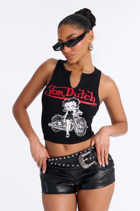 Woman in black crop top with red "Von Dutch" logo & Betty Boop on motorcycle, black leather shorts, studded belt, sunglasses.
