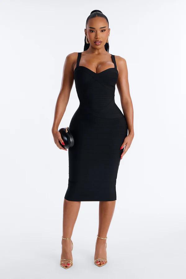 Woman in a black square-neck midi dress with a corseted bodice and draped skirt, holding an embellished black clutch, wearing strappy heels.