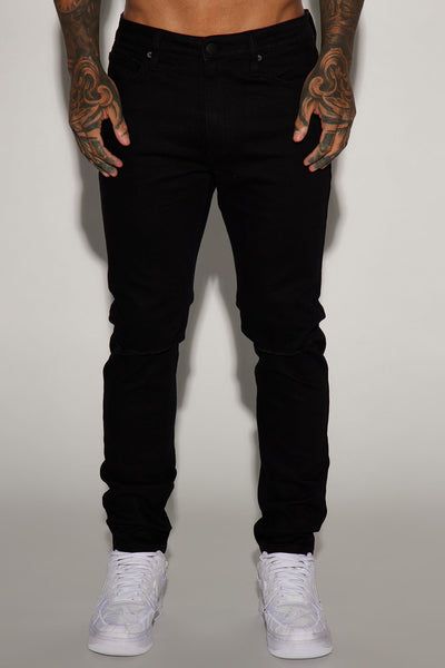 Waist-down shot of a man wearing dark black slim-fit jeans and crisp white sneakers. Highlights the sleek style and fit of men's modern denim.