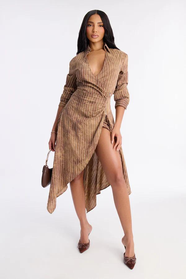 Woman in a sleeveless taupe midi dress featuring a distinctive waist design with a gold buckle, standing on a white background with clear heels.