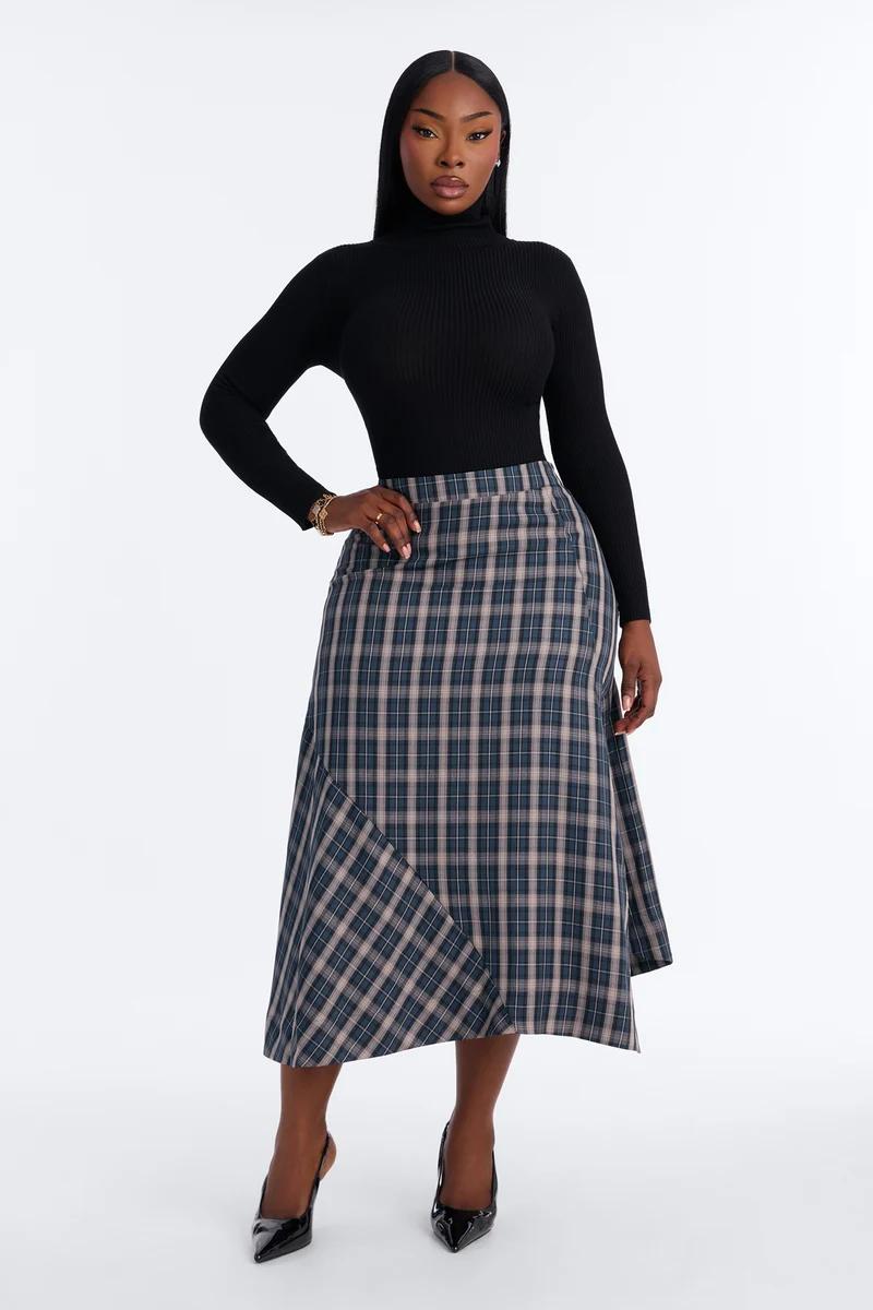 Modelo vistiendo un top negro de cuello alto y una falda midi asimétrica a cuadros azules de la nueva colección de moda de otoño para mujer.