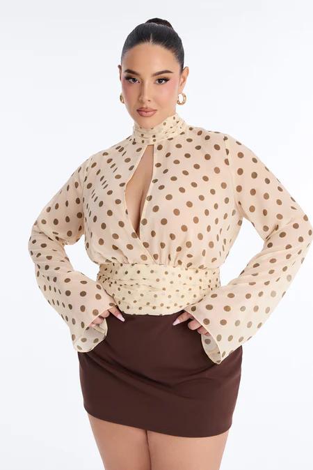 Mujer en blusa crema de lunares marrones con escote lágrima, mangas campana, cintura fruncida y minifalda marrón.