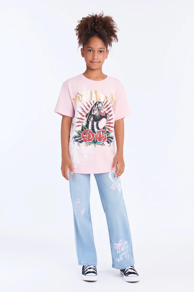 Niña con camiseta rosa con gráfico de pantera Ed Hardy y vaqueros azul claro estampados.
