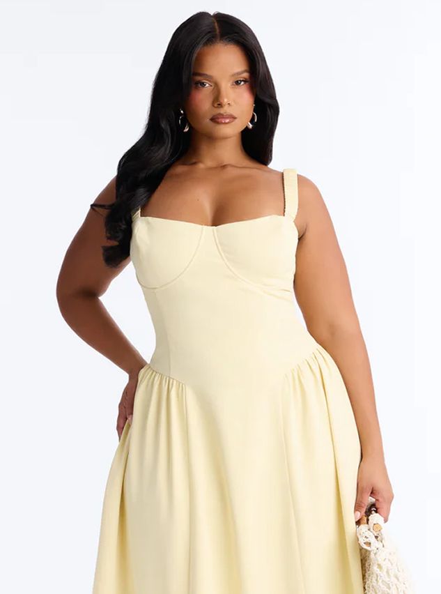 Model poses in a pastel yellow plus size dress with a sweetheart neckline and gathered skirt, highlighting stylish new summer apparel.