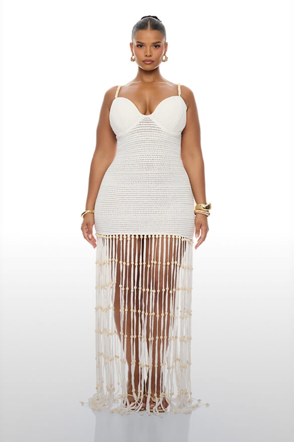 Elegant woman in white crochet maxi dress with fitted top and beaded fringe skirt, showcasing chic summer resort wear.