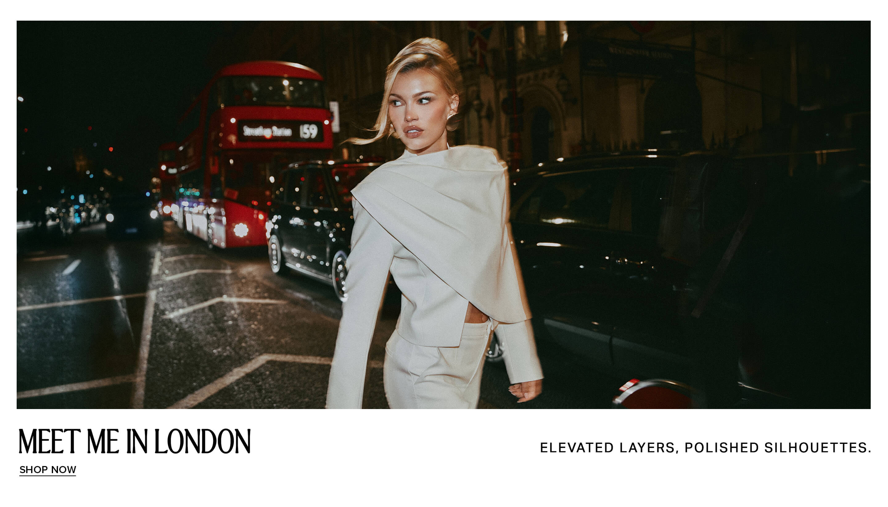 Blonde woman wears an elegant cream structured suit on a night London street with a red bus, promoting chic elevated layered fashion.