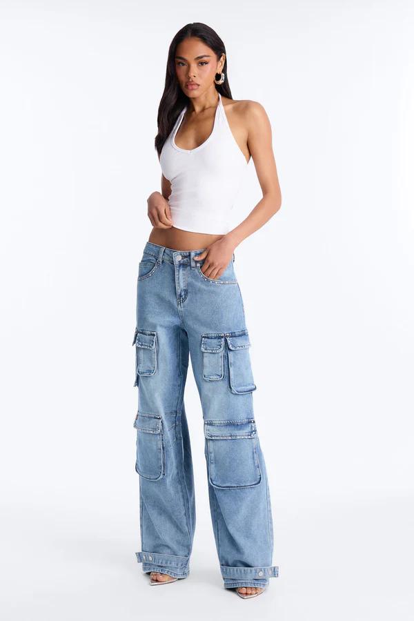 Woman in a white ribbed halter crop top and light blue wide-leg cargo jeans with rhinestone details, standing against a white background.