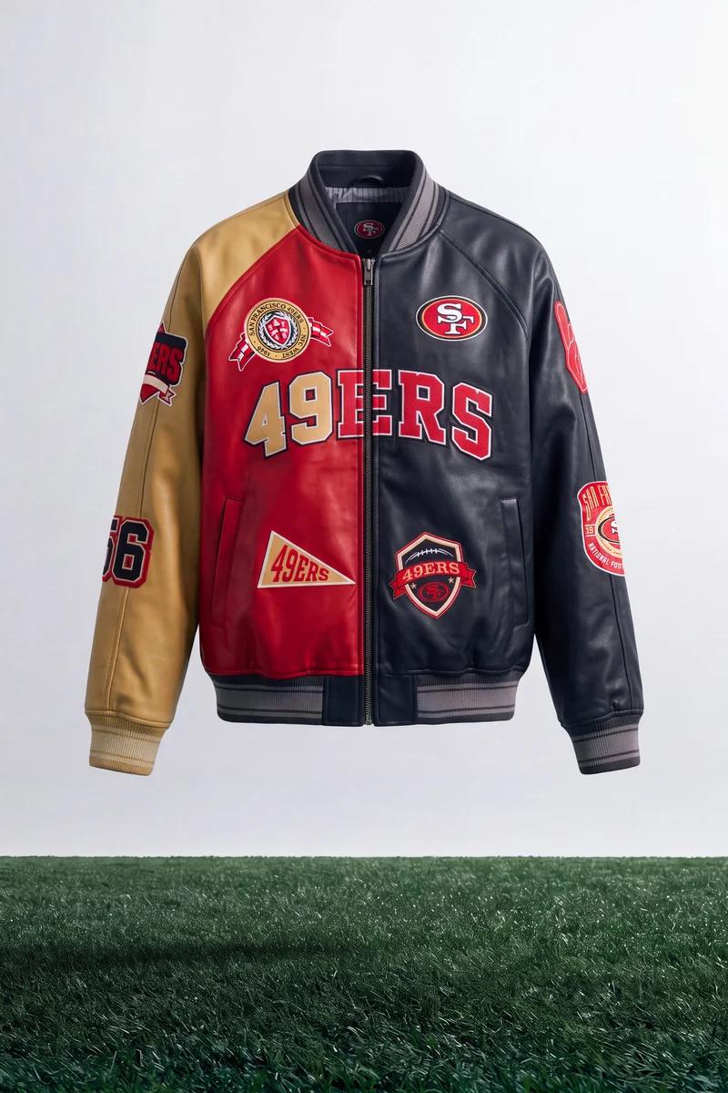 San Francisco 49ers bomber jacket: gold, red, black split design, featuring team logos & "49ERS" text, floating above grass.