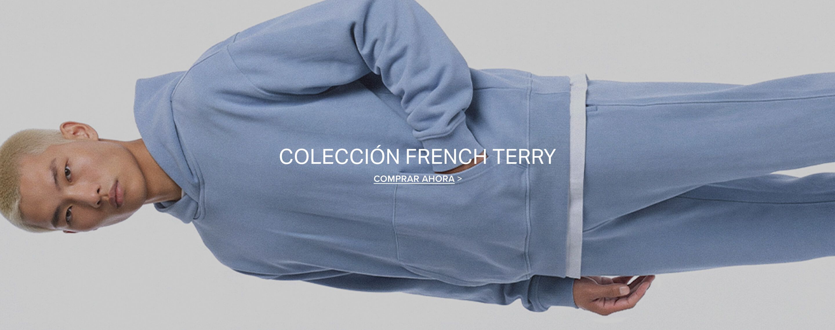 Modelo con sudadera azul de tejido French Terry sobre fondo gris. Banner de compra que promociona la nueva colección de ropa cómoda.