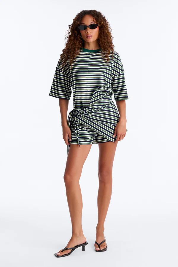 Model wears navy, green, white striped t-shirt and matching wrap shorts co-ord set with black sunglasses and sandals. Perfect casual summer outfit.