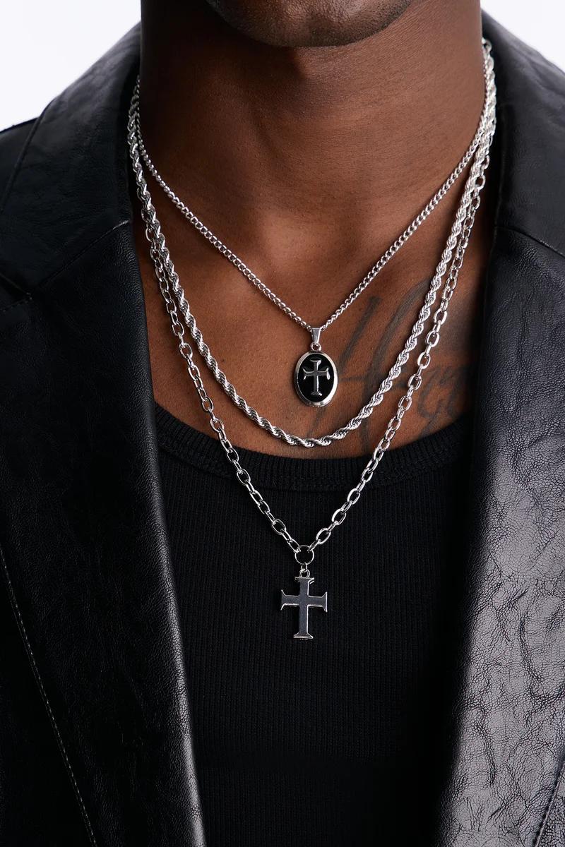 Hombre elegante con collares de plata superpuestos y dos colgantes de cruz negra. Explora nuestra colección de cadenas masculinas.