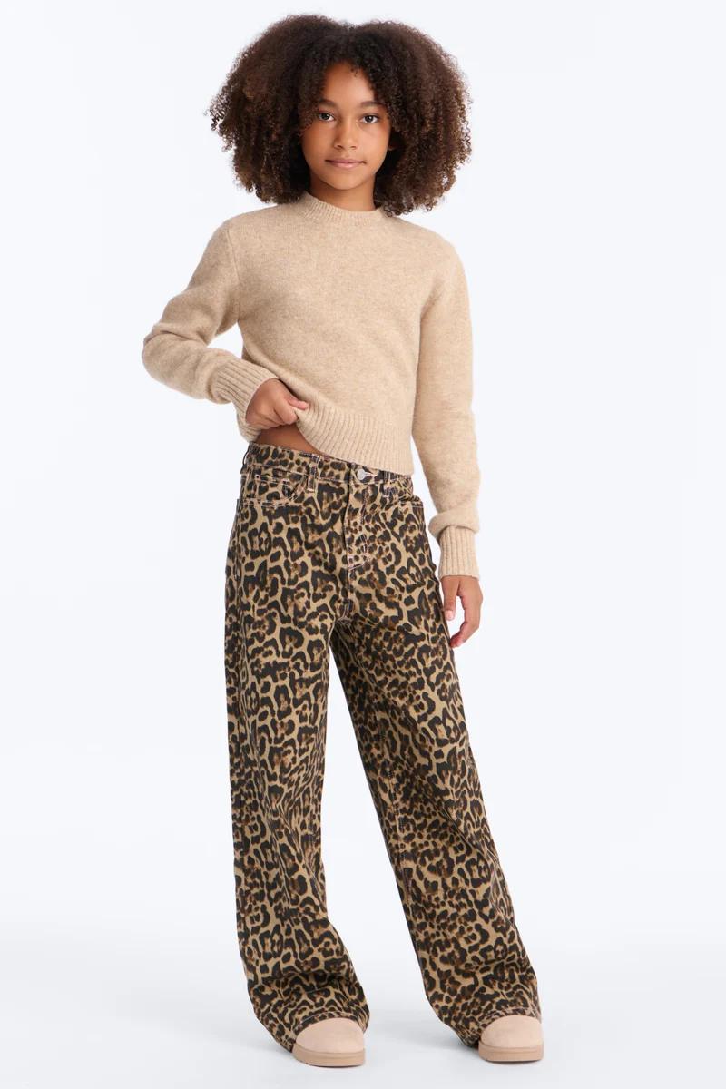Girl wearing a beige knit sweater and leopard print wide-leg jeans.