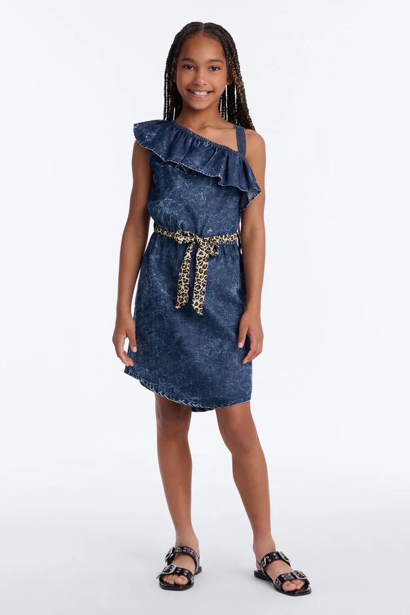 Smiling girl in ruffled one-shoulder acid wash denim dress with leopard print belt. Kids' fashion.