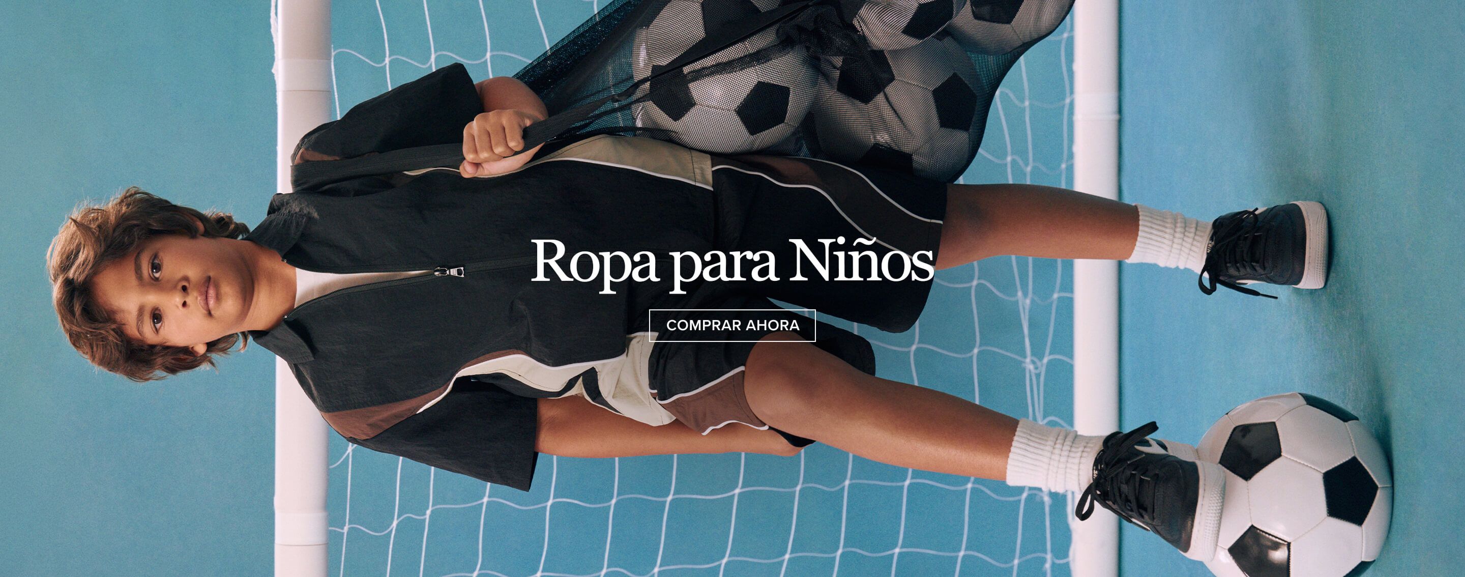 Joven con ropa deportiva negra y marrón, sostiene bolsa de balones de fútbol frente a red azul. Explora ropa de niño y moda deportiva ahora.