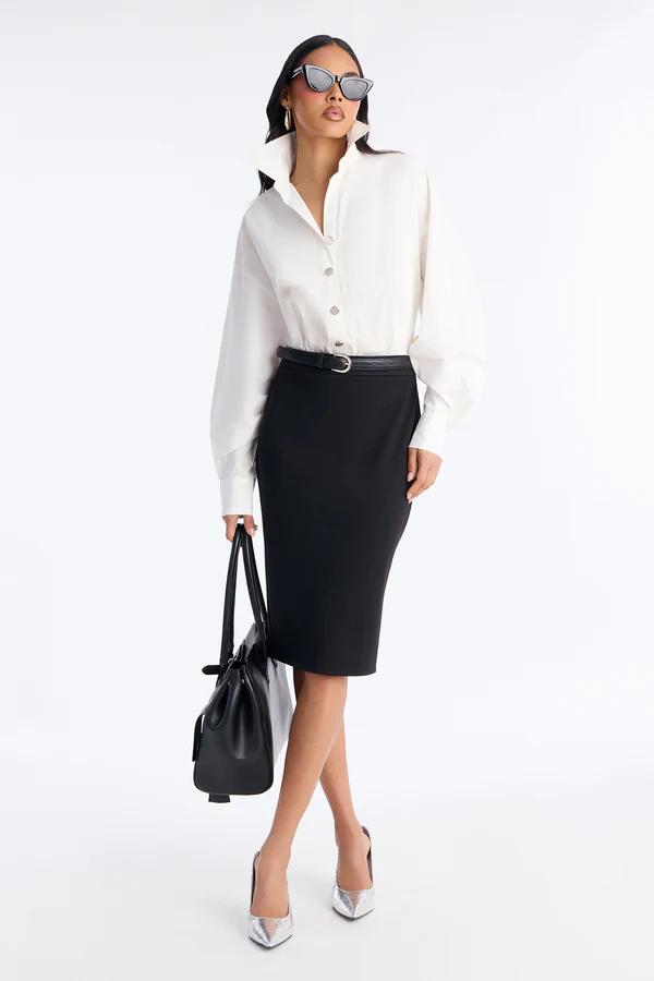 Woman in a sleeveless taupe midi dress featuring a distinctive waist design with a gold buckle, standing on a white background with clear heels.
