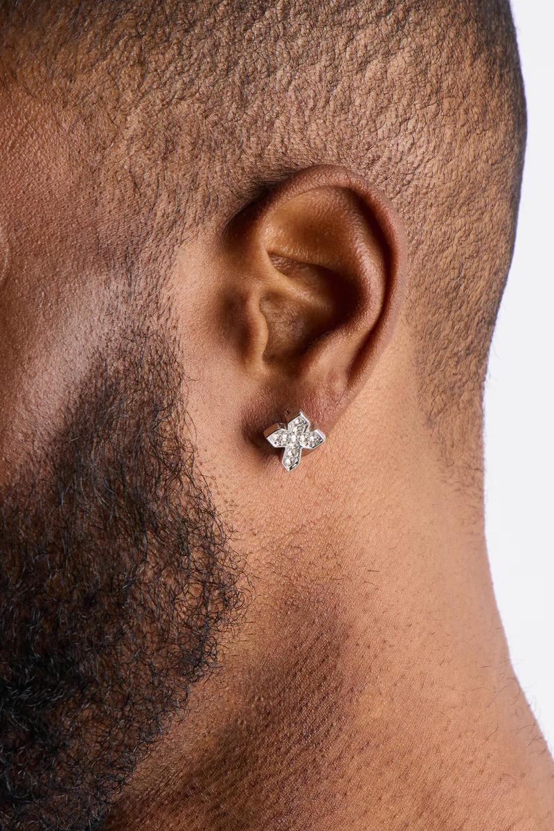 Primer plano de la oreja de un hombre con un brillante pendiente de cruz de plata con diamantes, destacando joyería masculina elegante.