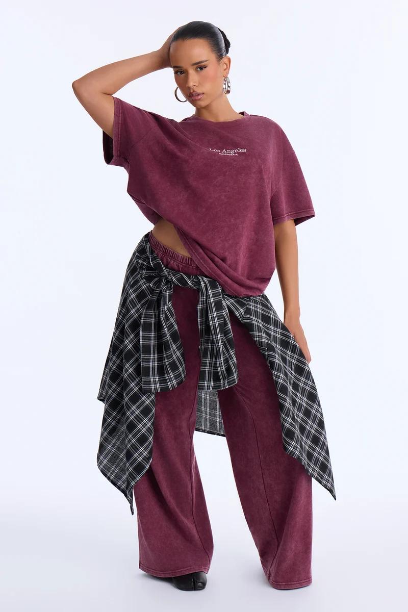 Model poses in a vintage plum burgundy oversized t-shirt and wide-leg lounge pants set styled with a black plaid shirt for a modern streetwear look.