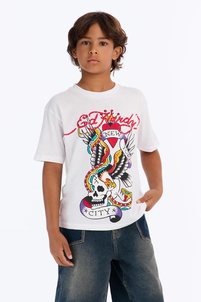 Boy in Ed Hardy white graphic t-shirt with eagle & snake, denim shorts, and white sneakers. Kids' streetwear fashion.