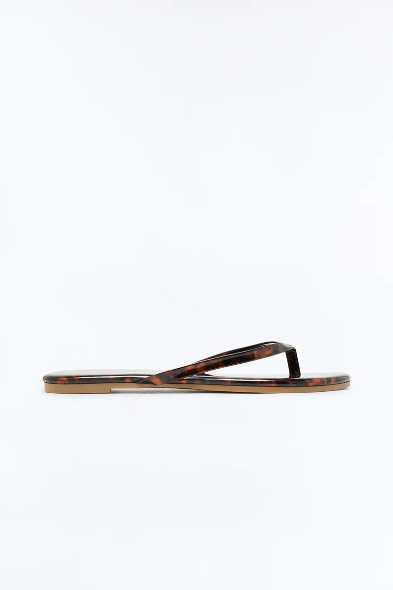 Single tortoiseshell flip-flop on a white background, featuring a glossy brown and black patterned strap and flat sole with a tan bottom.