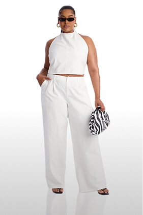 Stylish plus size woman in a crisp white halter crop top and wide-leg pleated pants co-ord, holding a chic zebra bag. Perfect for modern spring style.