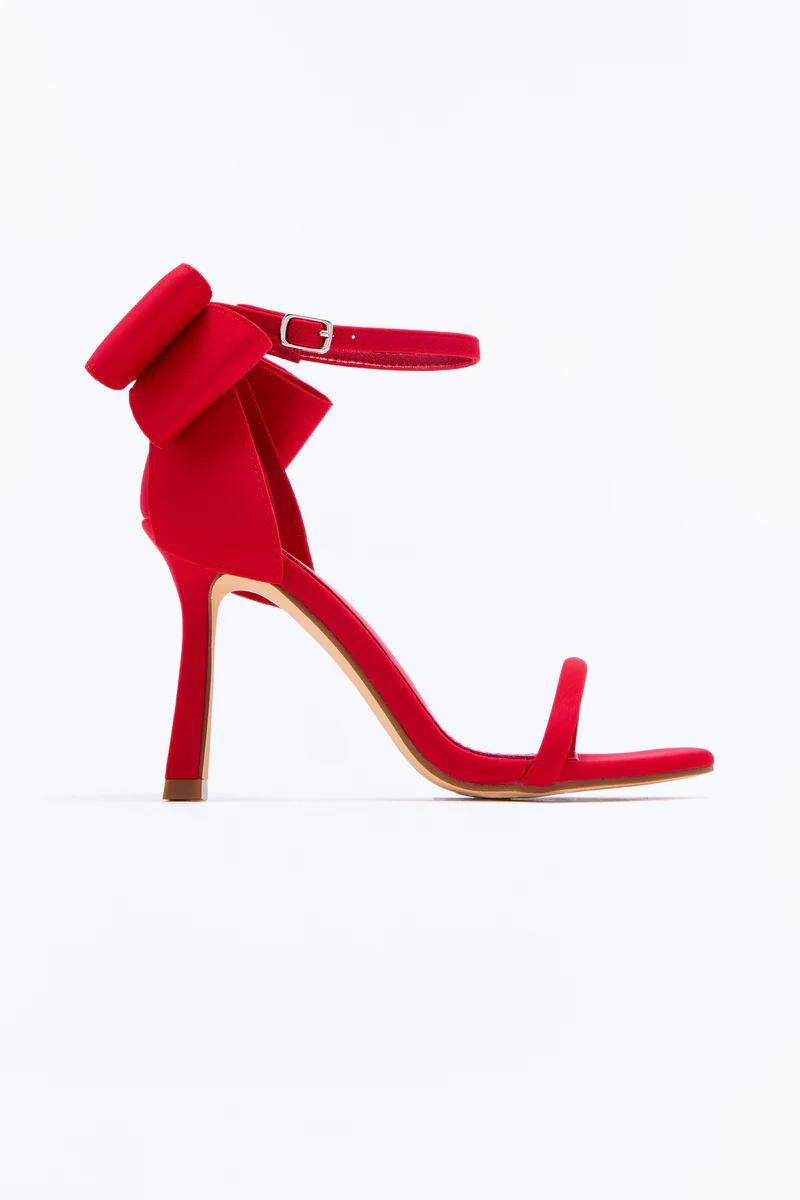Elegant red high heel sandals featuring a statement bow back, ankle strap, and stiletto heel.