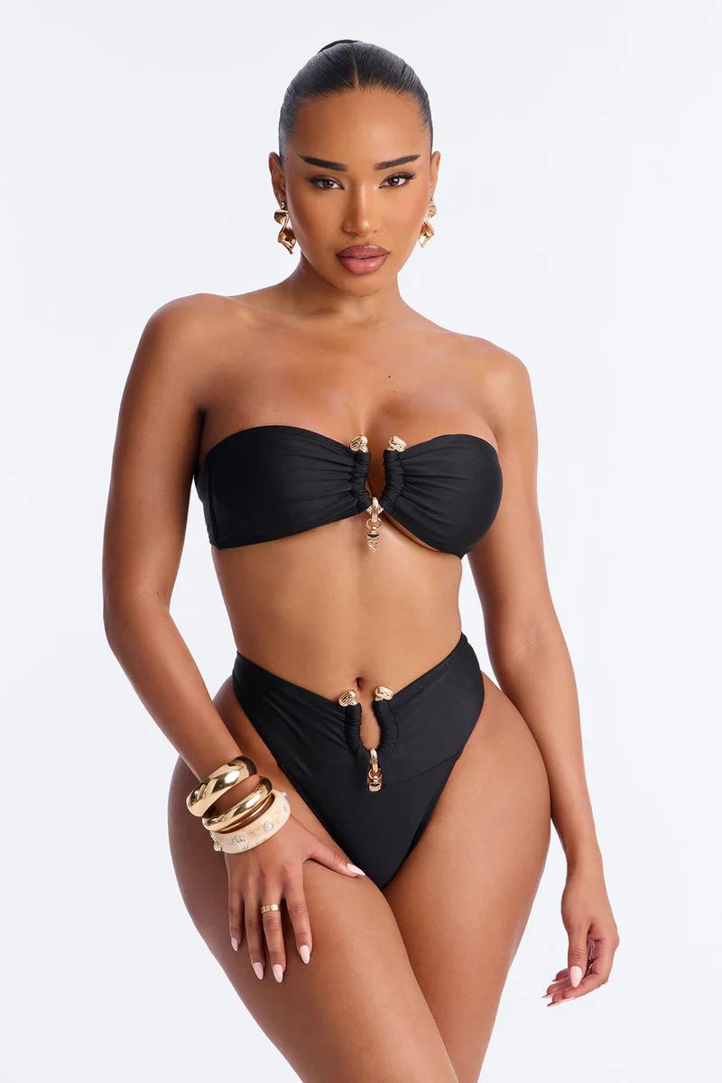 Confident woman models a chic black strapless bikini with gold hardware and high-waisted bottoms, showcasing a luxury swimwear.