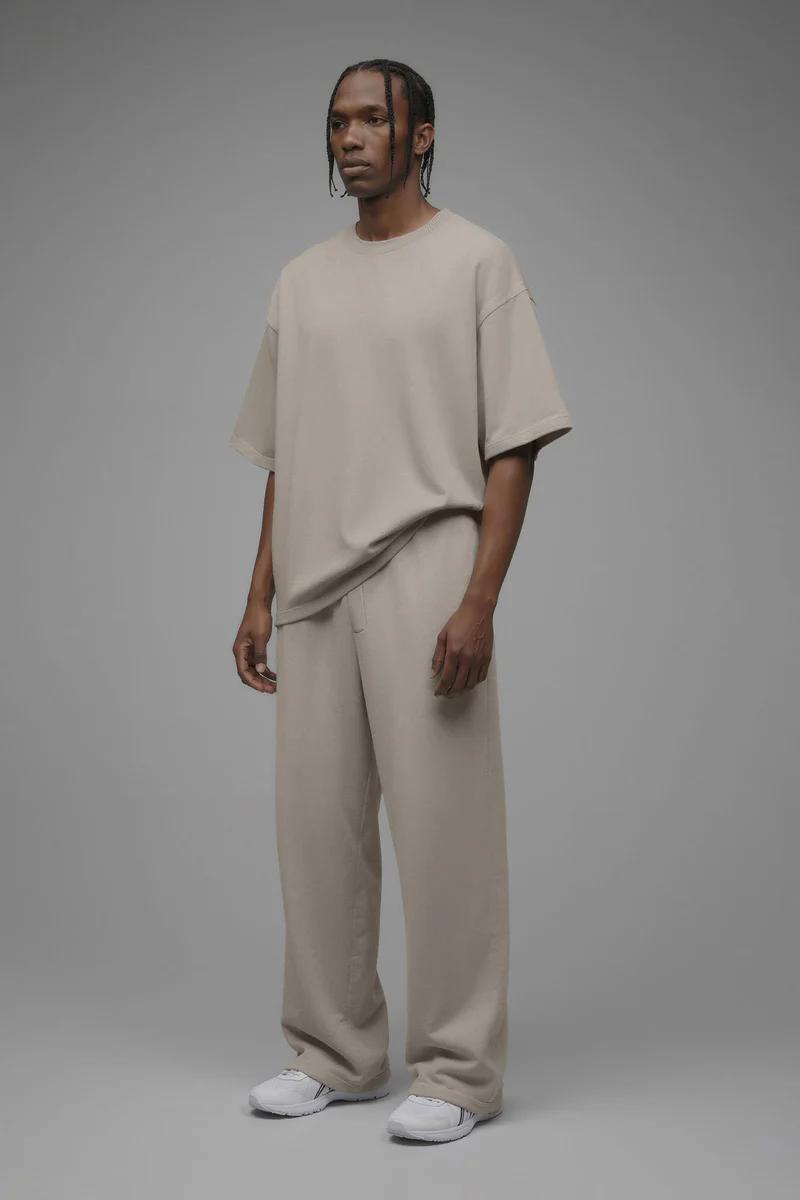 Man in a beige oversized t-shirt and matching wide-leg trousers, paired with white sneakers. Showcasing new men's casual comfort fashion.