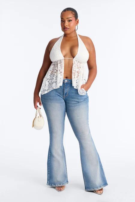 Mujer con halter de encaje blanco, vaqueros azules acampanados, tacones transparentes y bolso blanco pequeño, sobre fondo blanco.