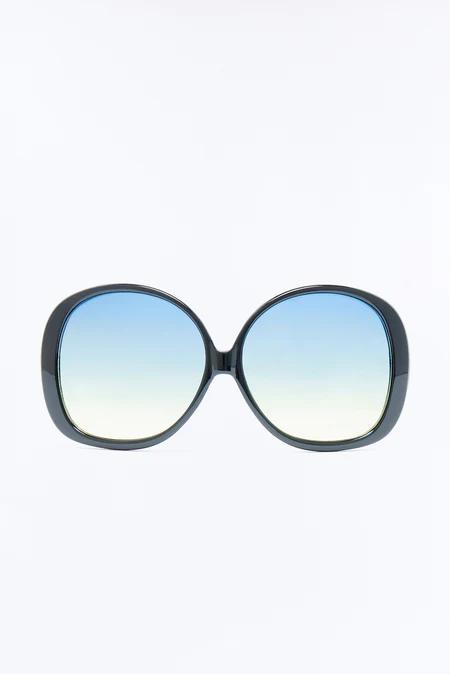 Elegantes gafas de sol grandes con montura gris oscuro. Los lentes redondos y amplios muestran un degradado azul a amarillo sobre un fondo blanco puro.