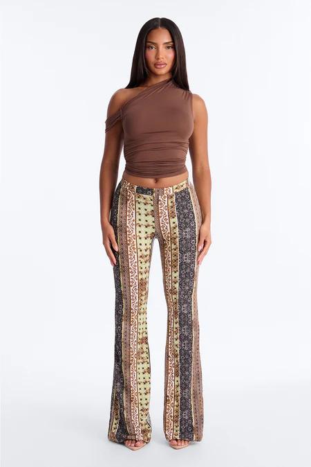 Mujer con top corto marrón de un solo hombro y pantalones acampanados de rayas verticales con estampados verdes, marrones y negros.