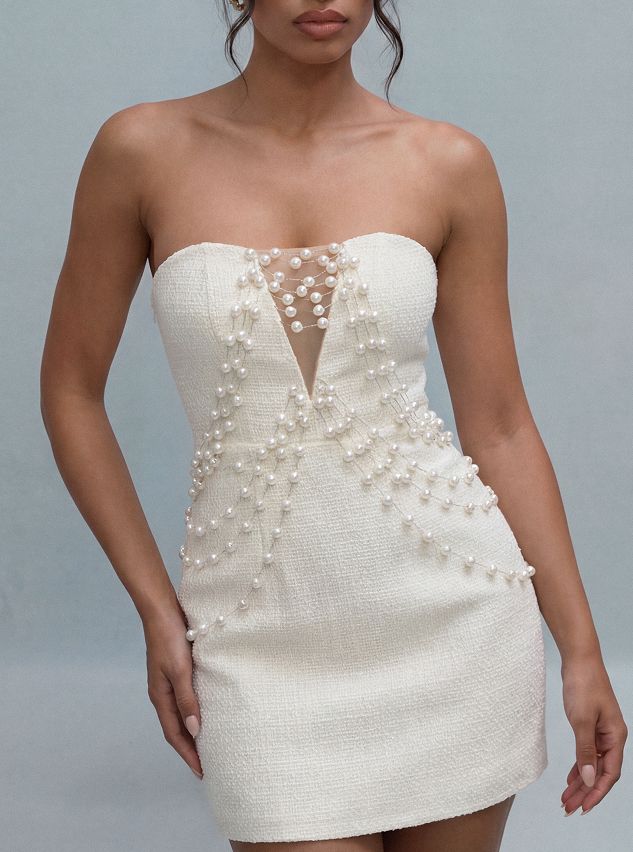 Elegante minivestido strapless color crema con deslumbrantes adornos de perlas en cascada sobre fondo azul claro. Ideal para noche.