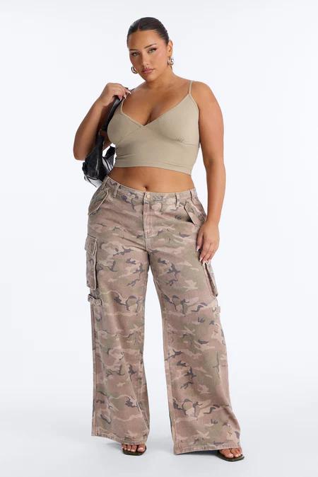 Mujer con top crop acanalado verde oliva y pantalones cargo anchos de camuflaje tenue, cargando un bolso negro.