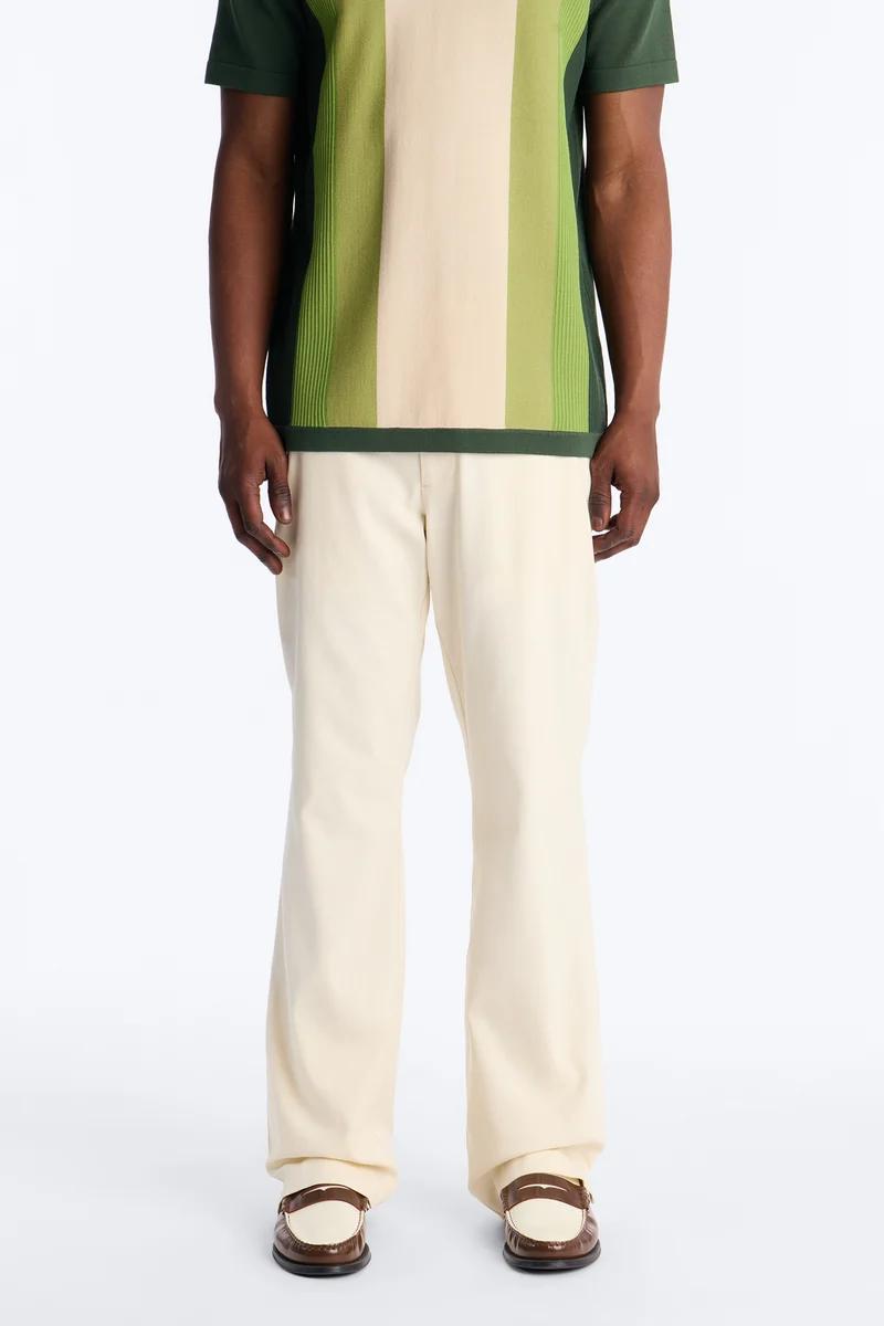 Hombre modela polo a rayas verde y crema, pantalones crema y mocasines marrones. Exhibiendo moda casual versátil para hombre.
