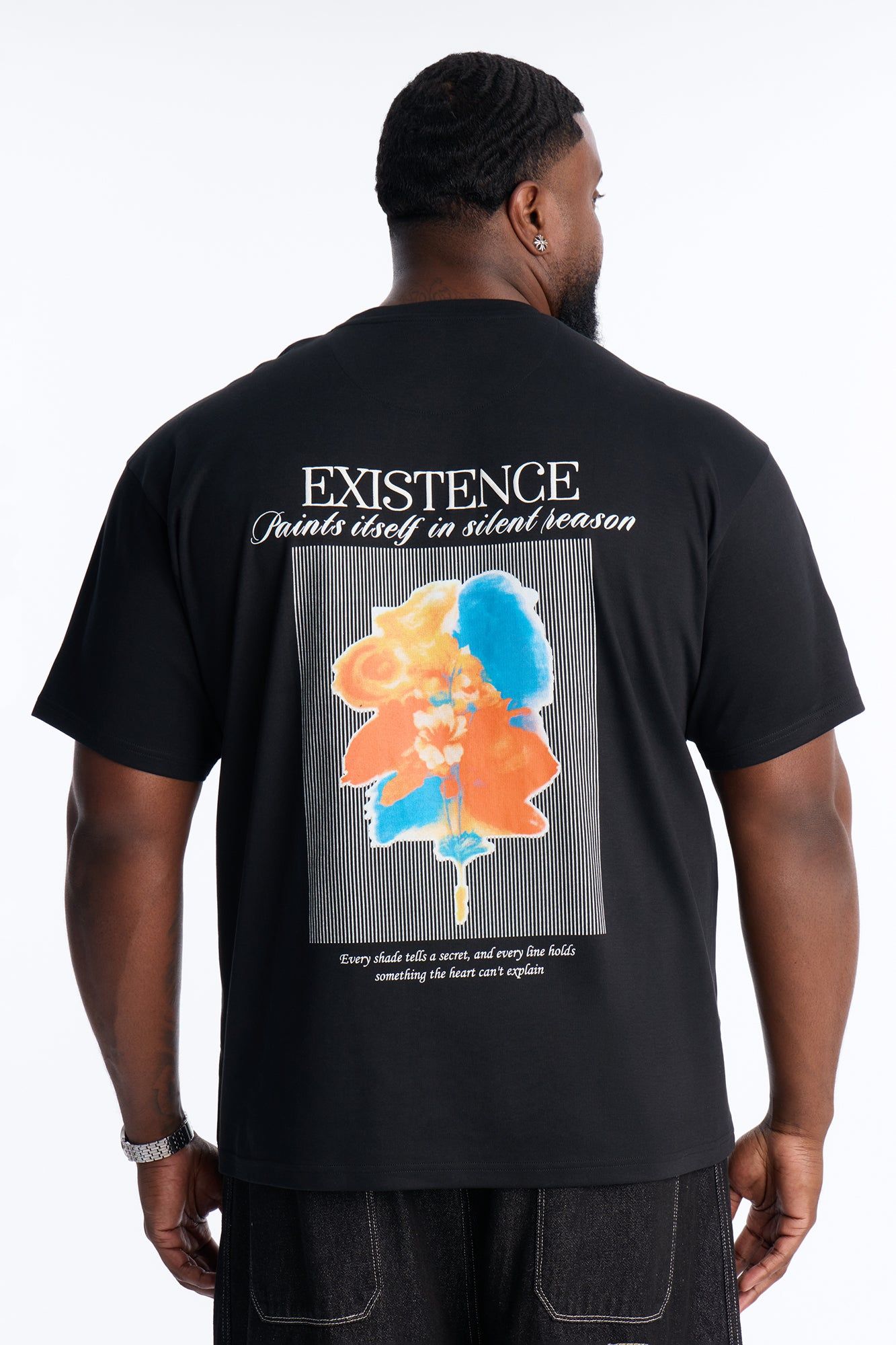 Back of a person wearing a black graphic t-shirt featuring "EXISTENCE" text and a vibrant abstract blue and orange floral design, promoting new casual men's apparel.