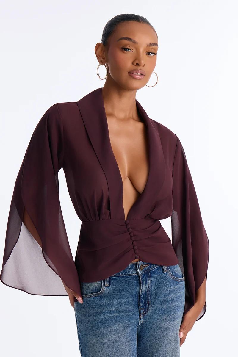 Woman wearing a deep V-neck burgundy blouse with flared long sleeves and button front.