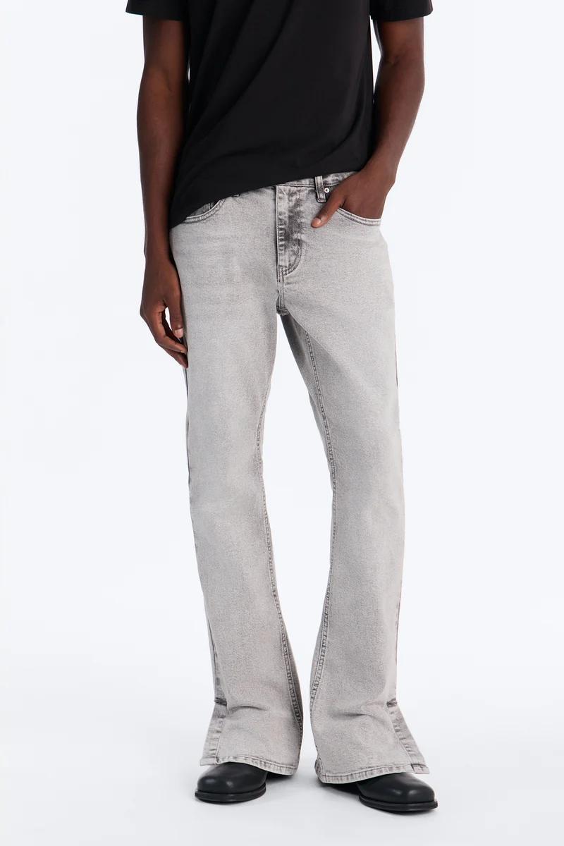 Man modeling light grey washed flared men's jeans with a black t-shirt and black shoes, showcasing stylish new denim collection.