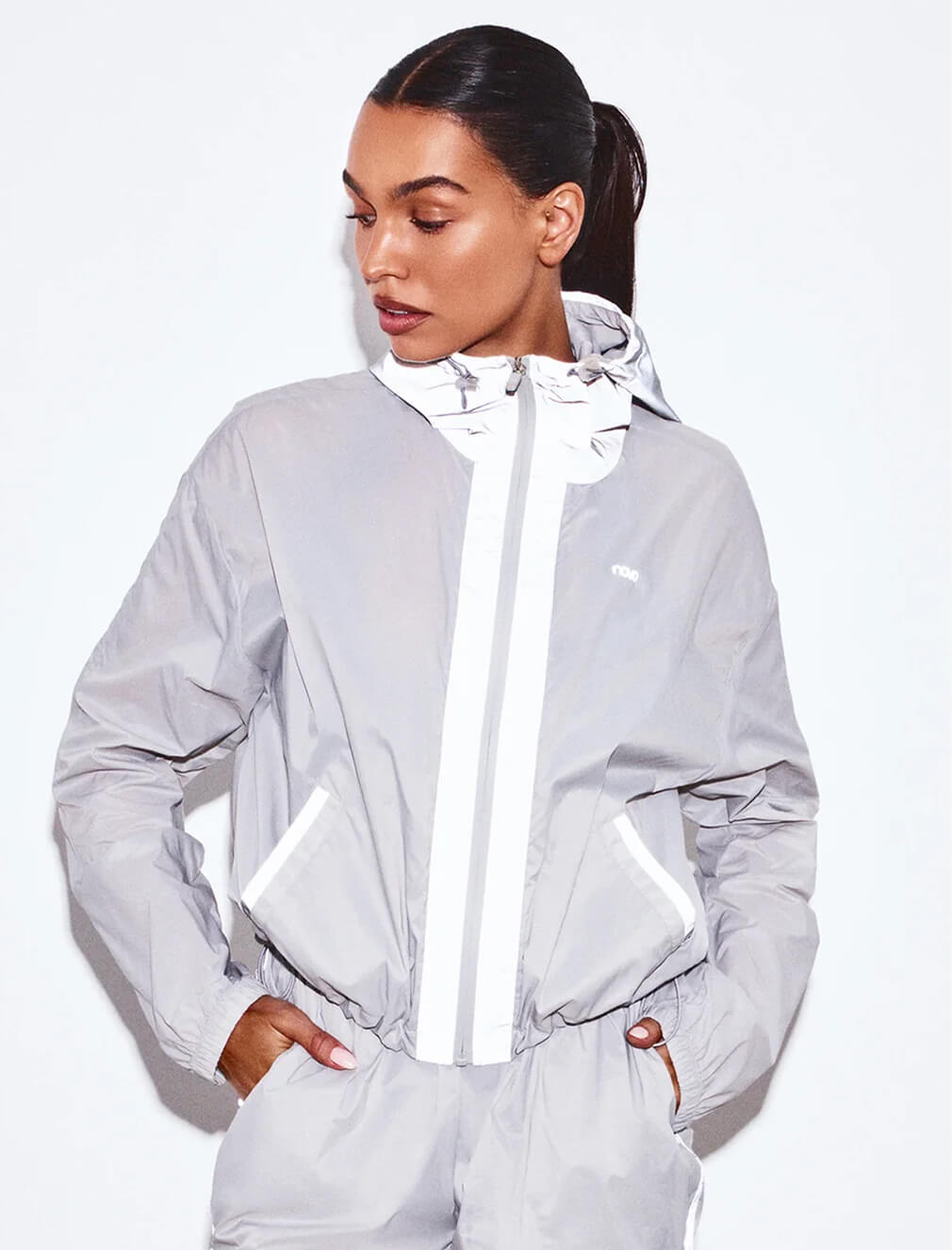 Woman wearing a lightweight women's grey windbreaker jacket with white details from a new activewear collection on a white background.