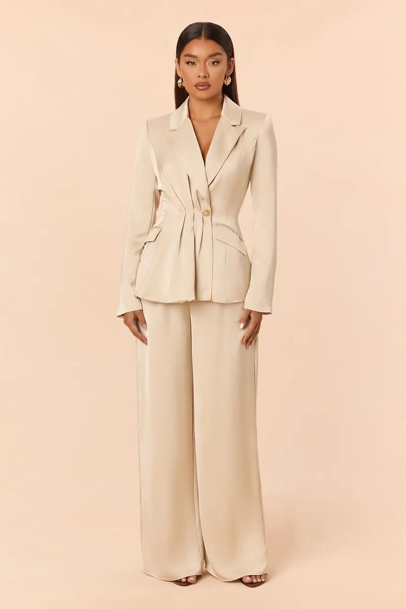 Elegant woman wearing a champagne satin pantsuit with a pleated cinched blazer and wide-leg trousers for a modern bridal or formal look.