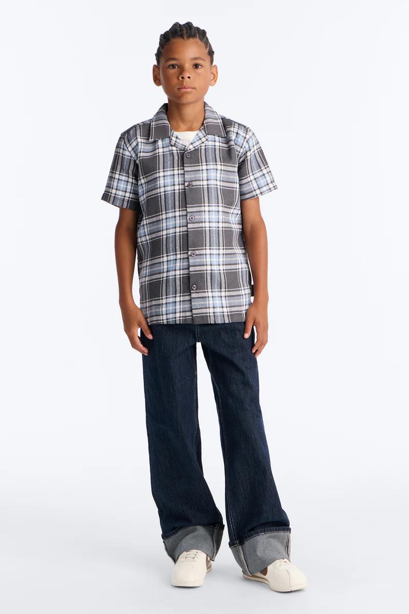 Niño con conjunto de camisa y shorts de rizo verde oliva, estampado paisley, camiseta blanca, zapatillas. Moda casual infantil de verano.