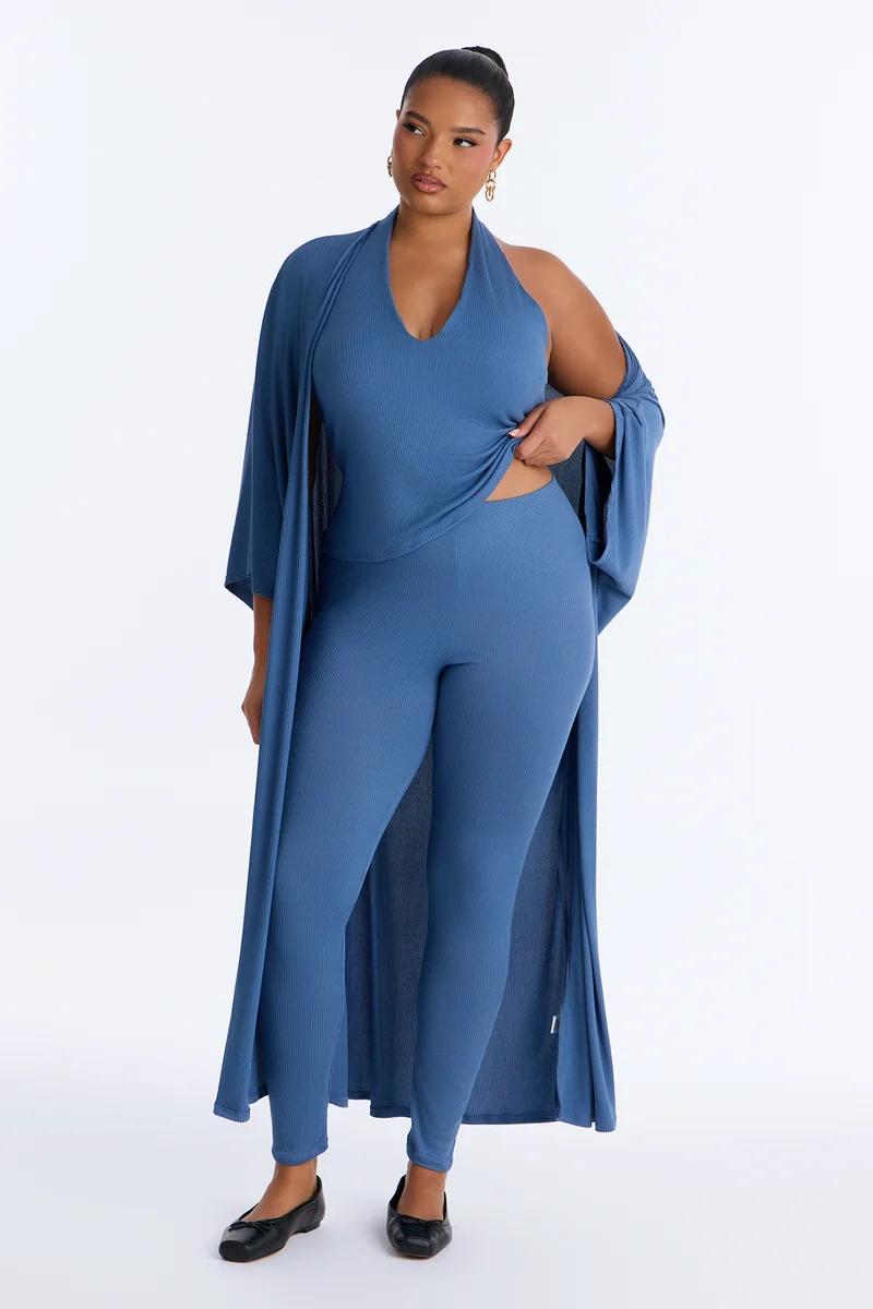 Plus-size model posing in a slate blue ribbed 3-piece loungewear set featuring a halter top, leggings, and a long matching open cardigan.