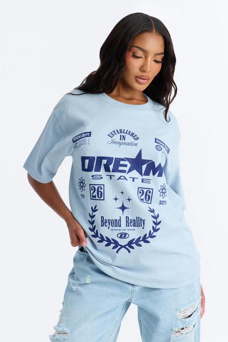 Woman wearing an oversized light blue graphic t-shirt featuring "DREAM STATE" and "Beyond Reality" text, paired with light blue ripped jeans.