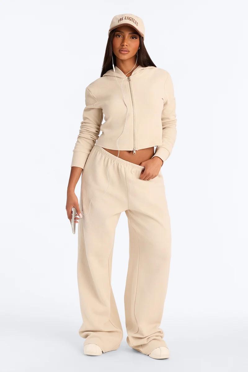 Woman models a monochrome beige cropped zip-up hoodie and matching wide-leg sweatpants set, promoting trendy women's casual streetwear.
