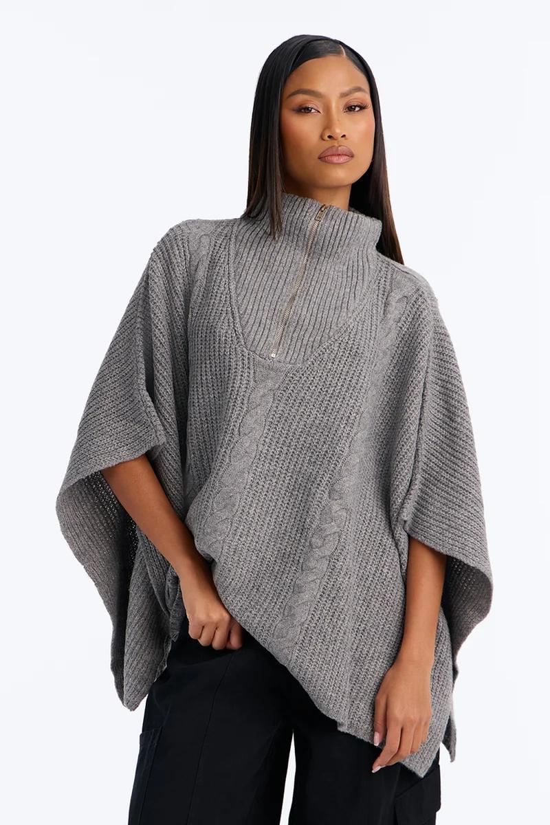 Woman wearing a grey cable knit poncho sweater with a half-zip turtleneck.