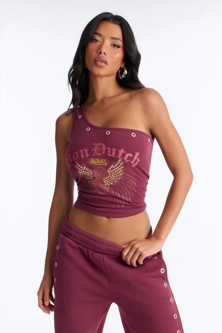 Woman posing in a maroon one-shoulder crop top with silver grommets and a "Von Dutch" winged logo, paired with matching grommeted joggers.