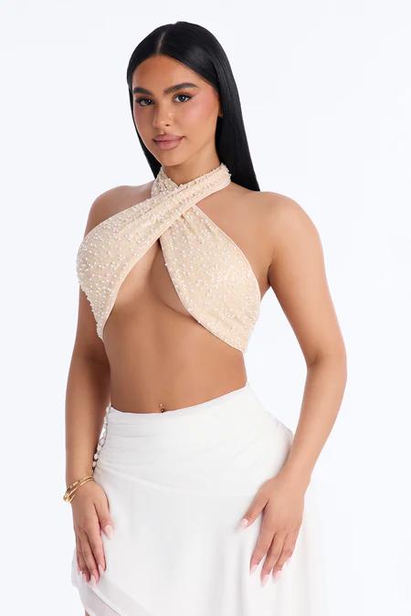 Mujer de cabello oscuro con top halter champán con cuentas y falda blanca fluida, posando con confianza sobre un fondo blanco limpio.