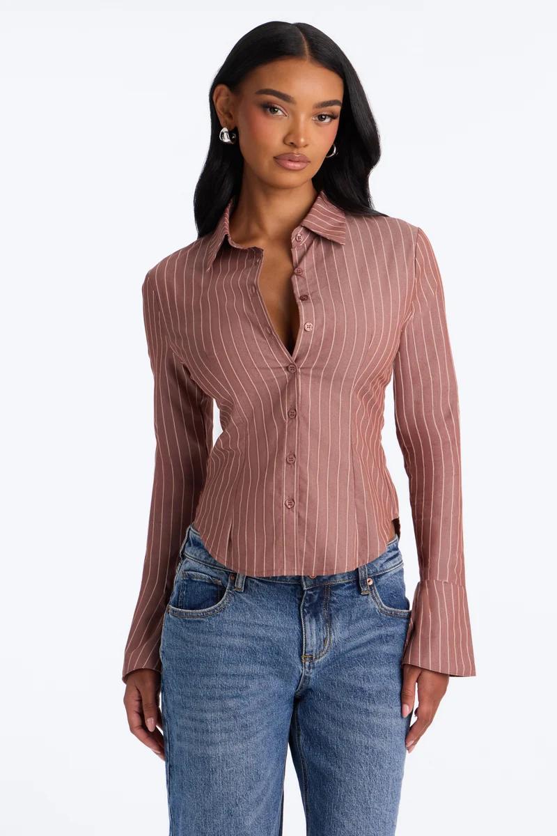 Woman wearing a dusty rose pinstripe long sleeve button-up shirt and blue jeans.