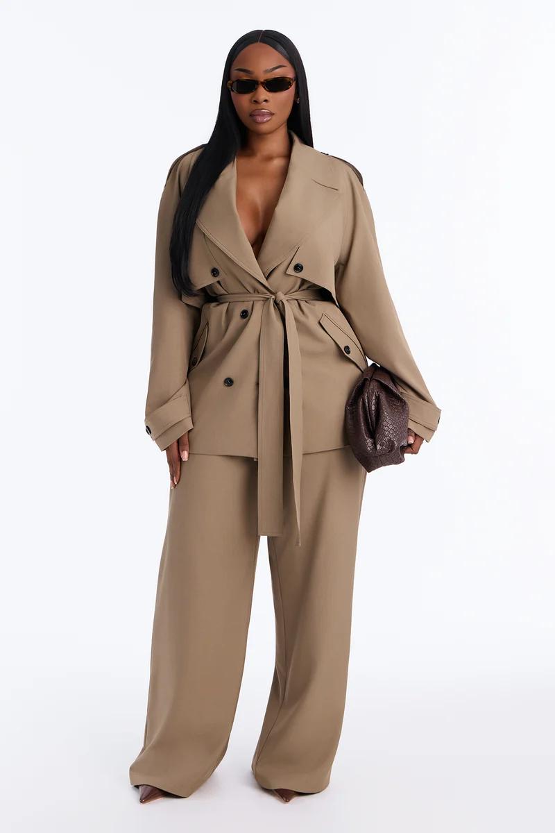 Stylish woman wearing a beige belted trench jacket and matching wide-leg trousers with a brown clutch for a chic autumn suit collection.